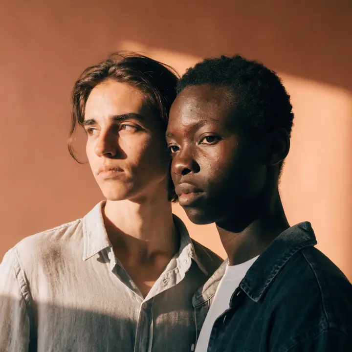 A couple standing cheek to cheek in warm sunlight against a terracotta wall